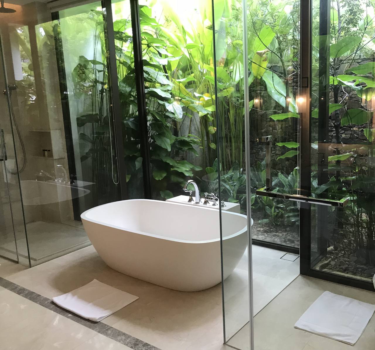 free standing bath sits aside a glass wall behind which is a luxurious garden